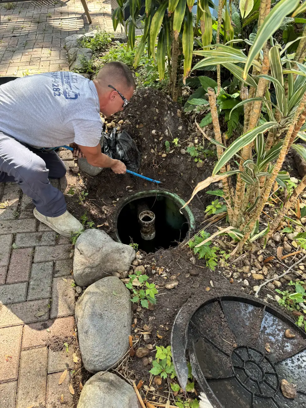 Tech servicing a septic riser in a planted bed